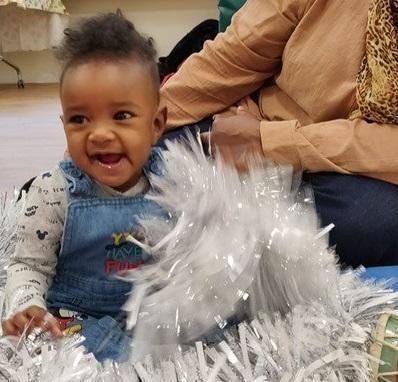 Image depicts a baby sitting in a pile of tinsel