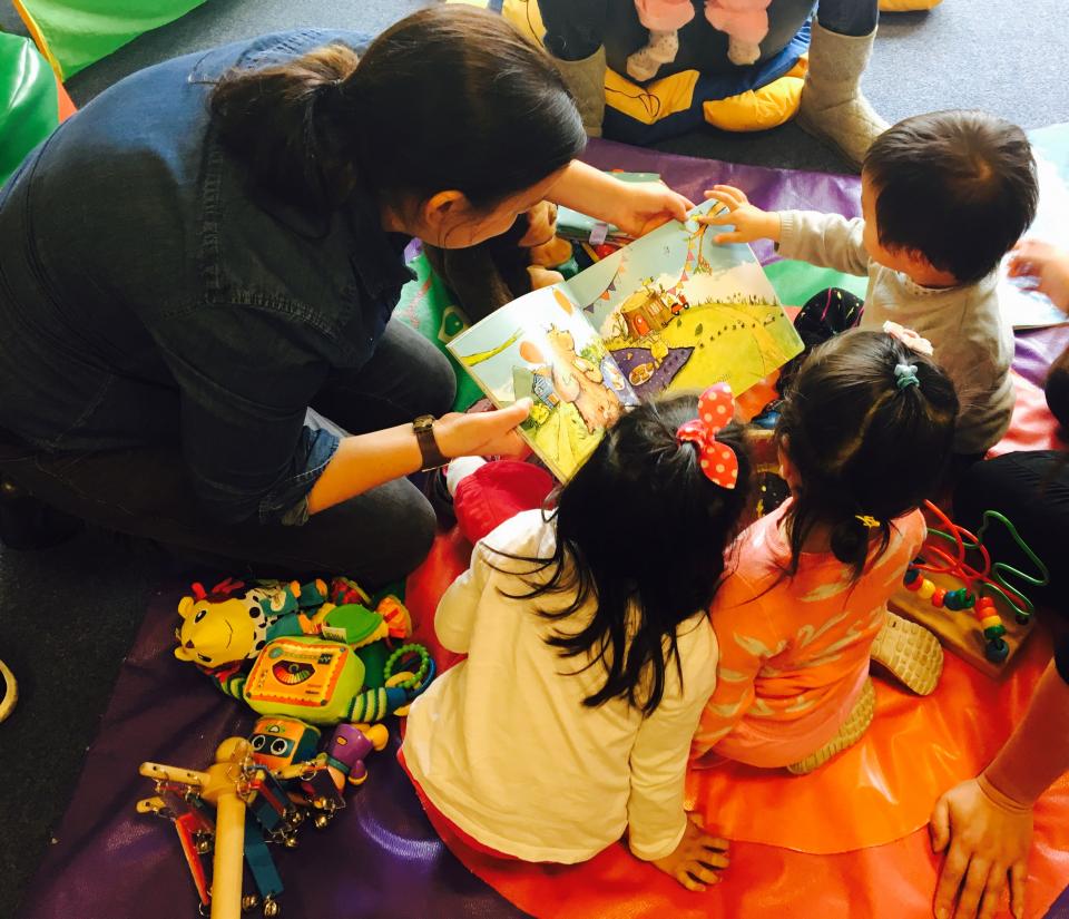 A story time during one of our Early Years groups. A grown-up holds a kids' book while three children look on and enjoy. 