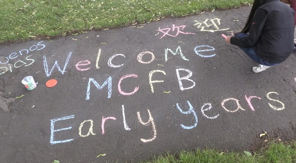 An overhead image of a colorful chalk drawing that reads "Welcome MCFB Early Years". There are also some greetings written in chalk around the edges.